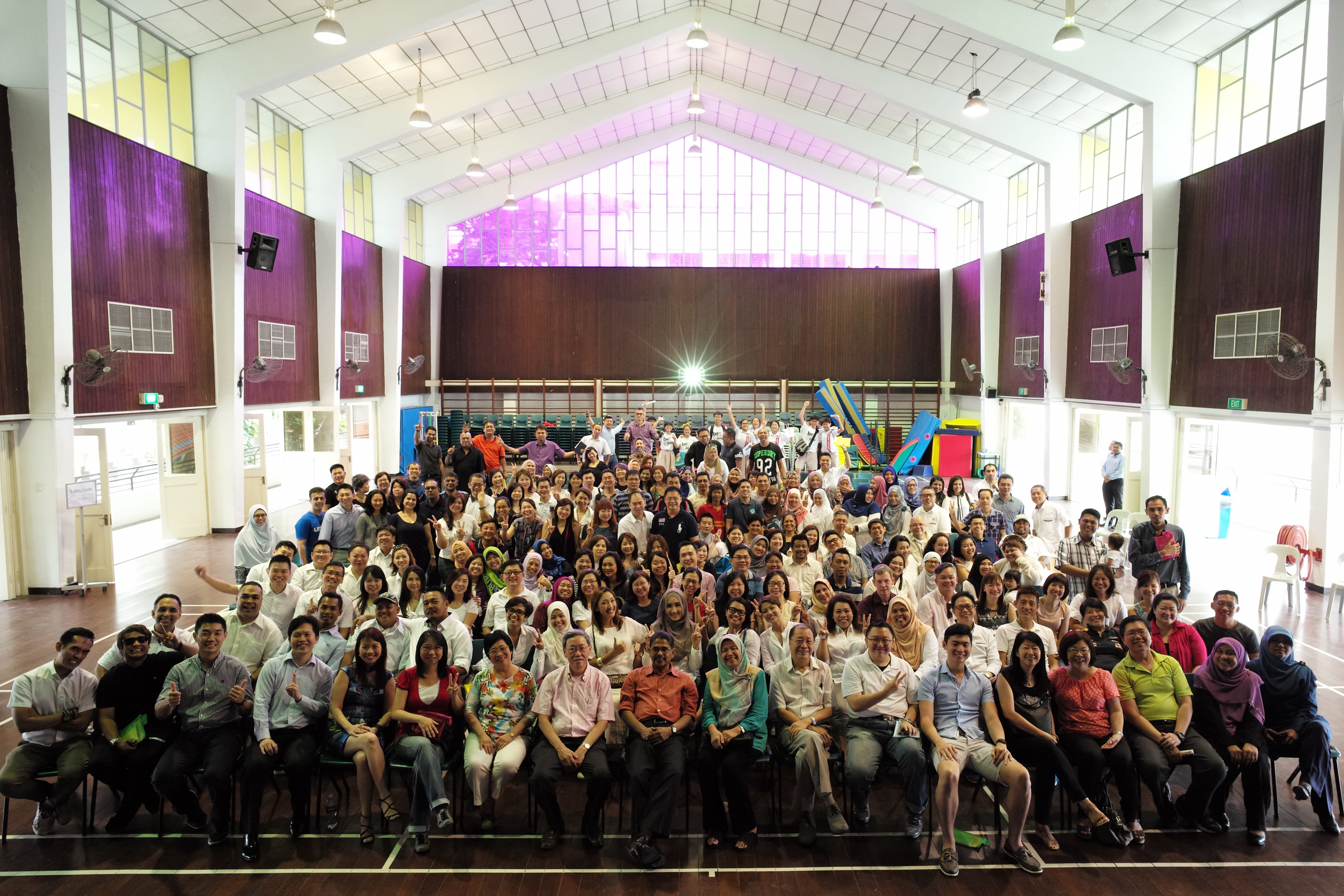 Large group of people posing for a photo inside a hall with purple walls and a vaulted ceiling.